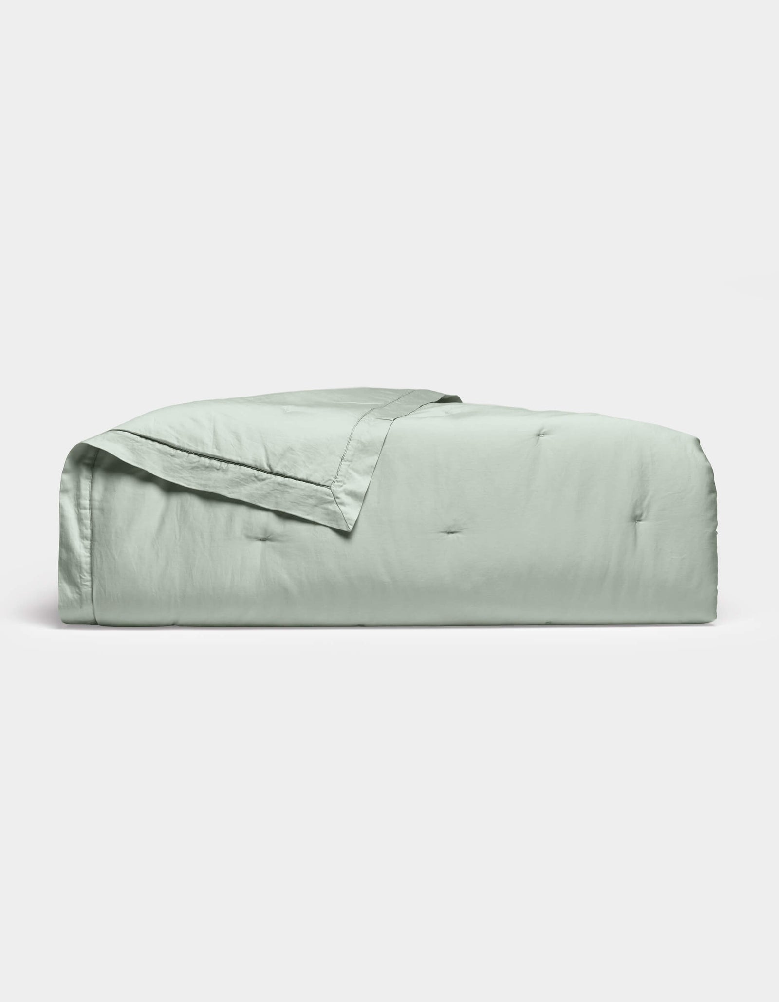 The Soft-Wash Cotton Quilt by Cozy Earth, in light green with a stitched edge, is neatly folded and displayed on a plain white background.