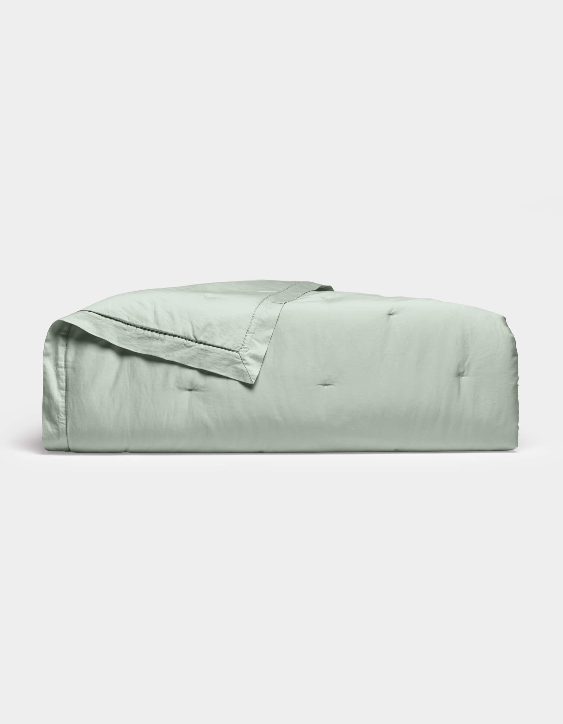 The Soft-Wash Cotton Quilt by Cozy Earth, in light green with a stitched edge, is neatly folded and displayed on a plain white background.|Color:Laurel