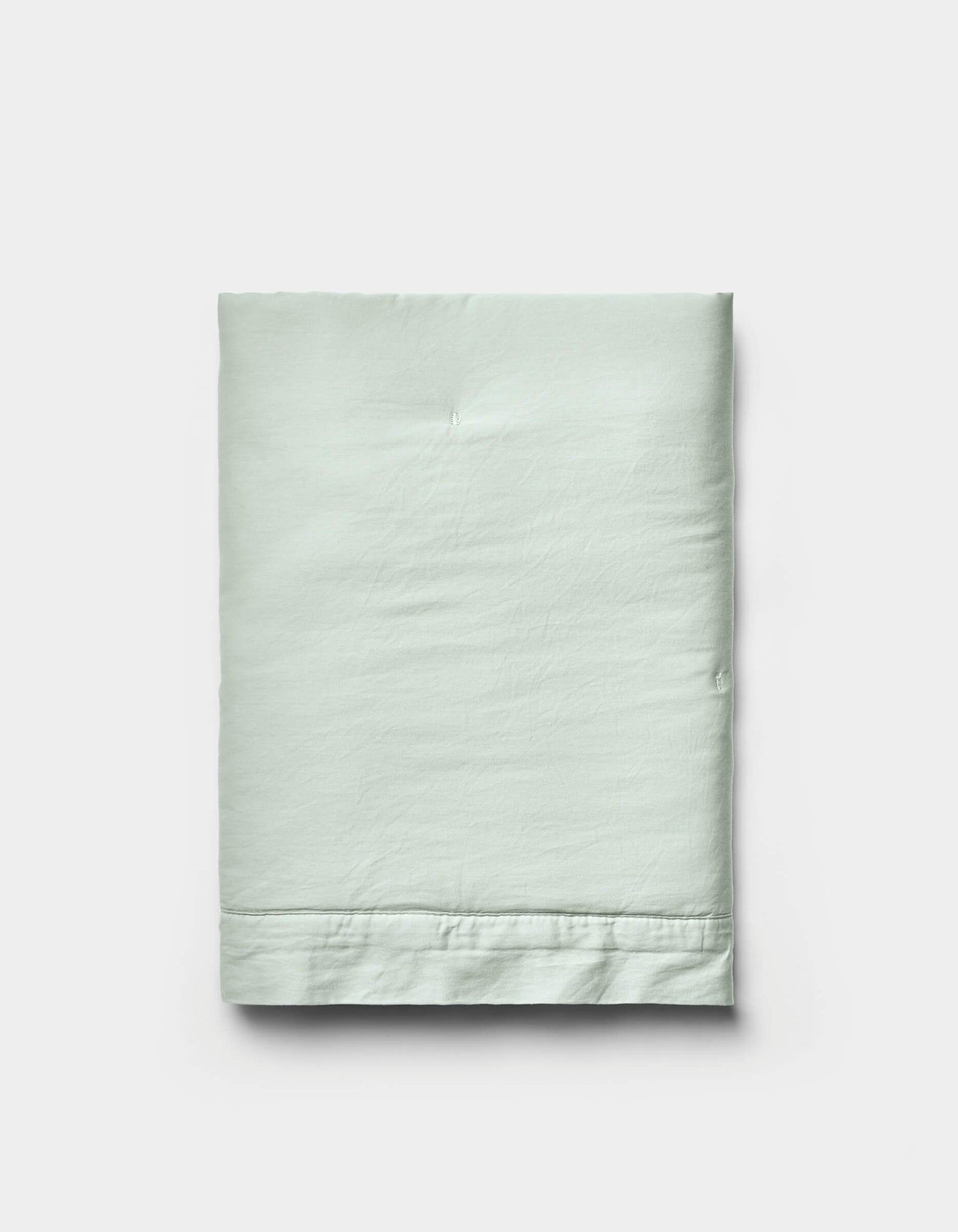 A neatly folded Soft-Wash Cotton Quilted Sham by Cozy Earth in light green is displayed on a plain white background, showcasing its smooth texture and visible stitched hem near the bottom edge.