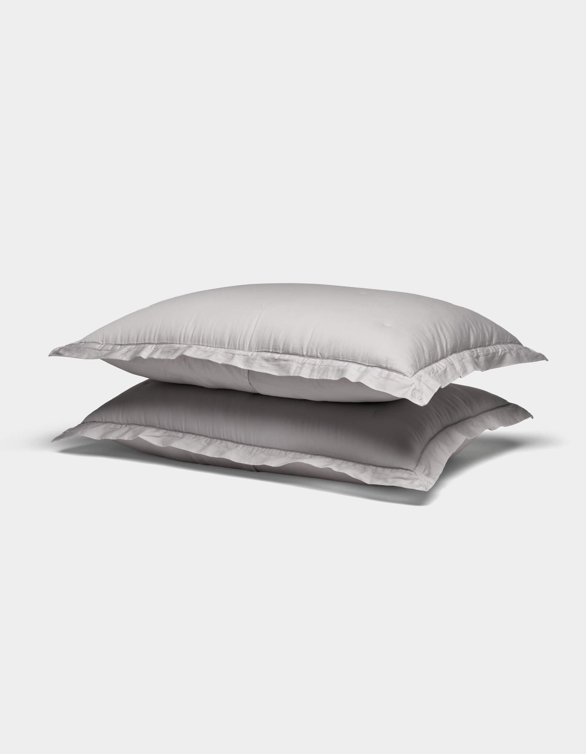 Two Soft-Wash Cotton Shams by Cozy Earth in white are stacked atop one another against a plain light gray background.|Color:Dew