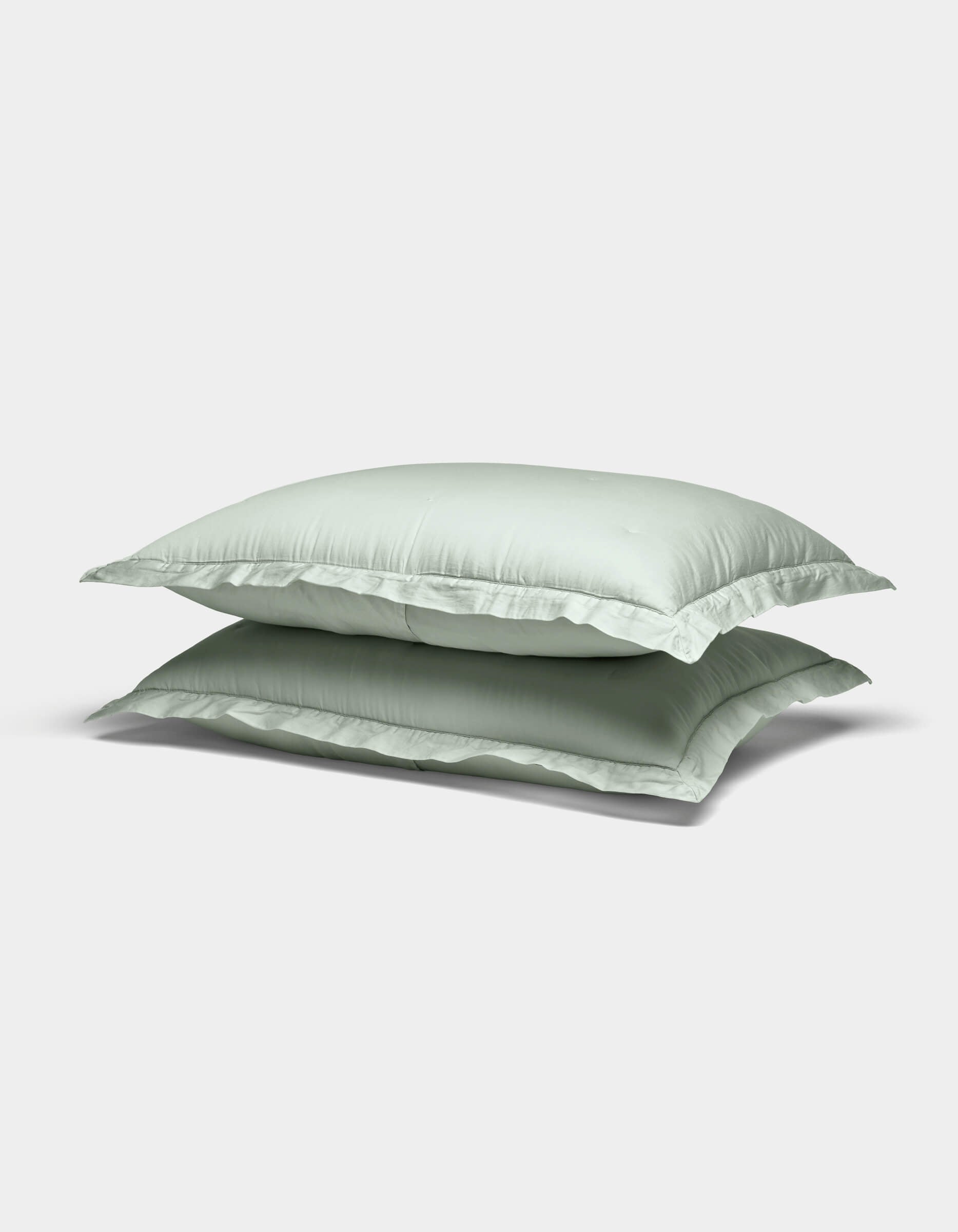Two Soft-Wash Cotton Shams by Cozy Earth in light green are stacked atop each other against a plain white background.|Color:Laurel