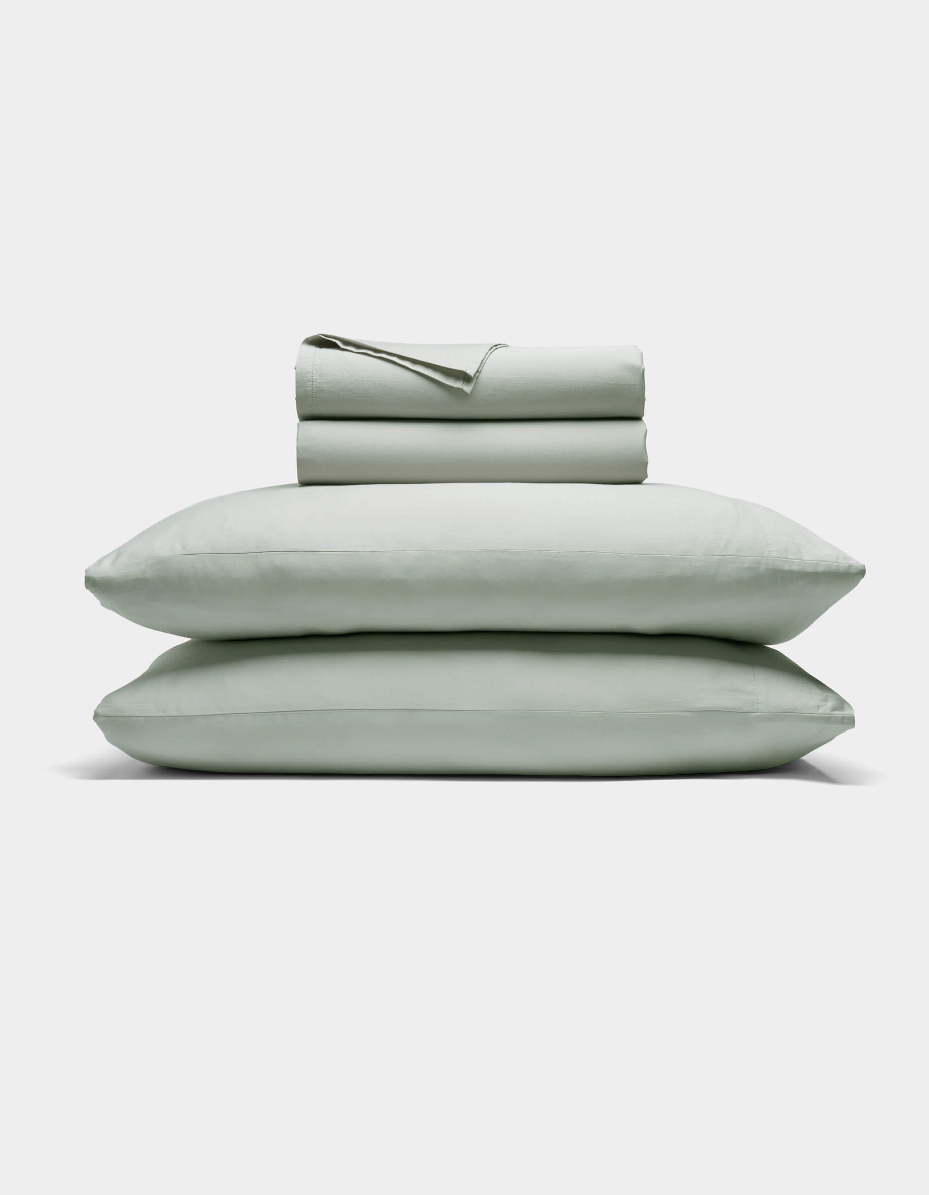 The Cozy Earth Soft-Wash Cotton Sheet Set includes a neatly folded light gray fitted and flat sheet with two stacked pillows, displayed against a plain white background.|Color:Laurel