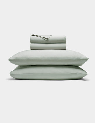 The Cozy Earth Soft-Wash Cotton Sheet Set includes a neatly folded light gray fitted and flat sheet with two stacked pillows, displayed against a plain white background.|Color:Laurel