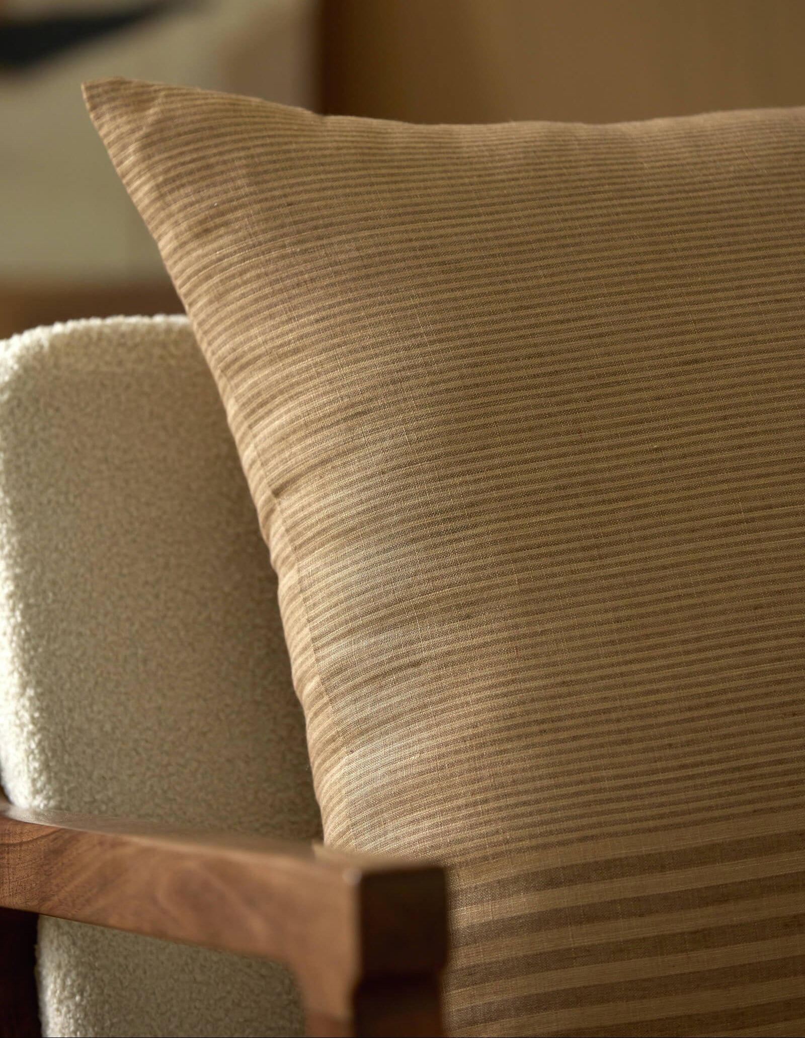 A close-up of the Cozy Earth Striped Throw Pillow resting against a light upholstered chair with a wooden frame. The softly blurred background creates a warm, inviting ambiance.