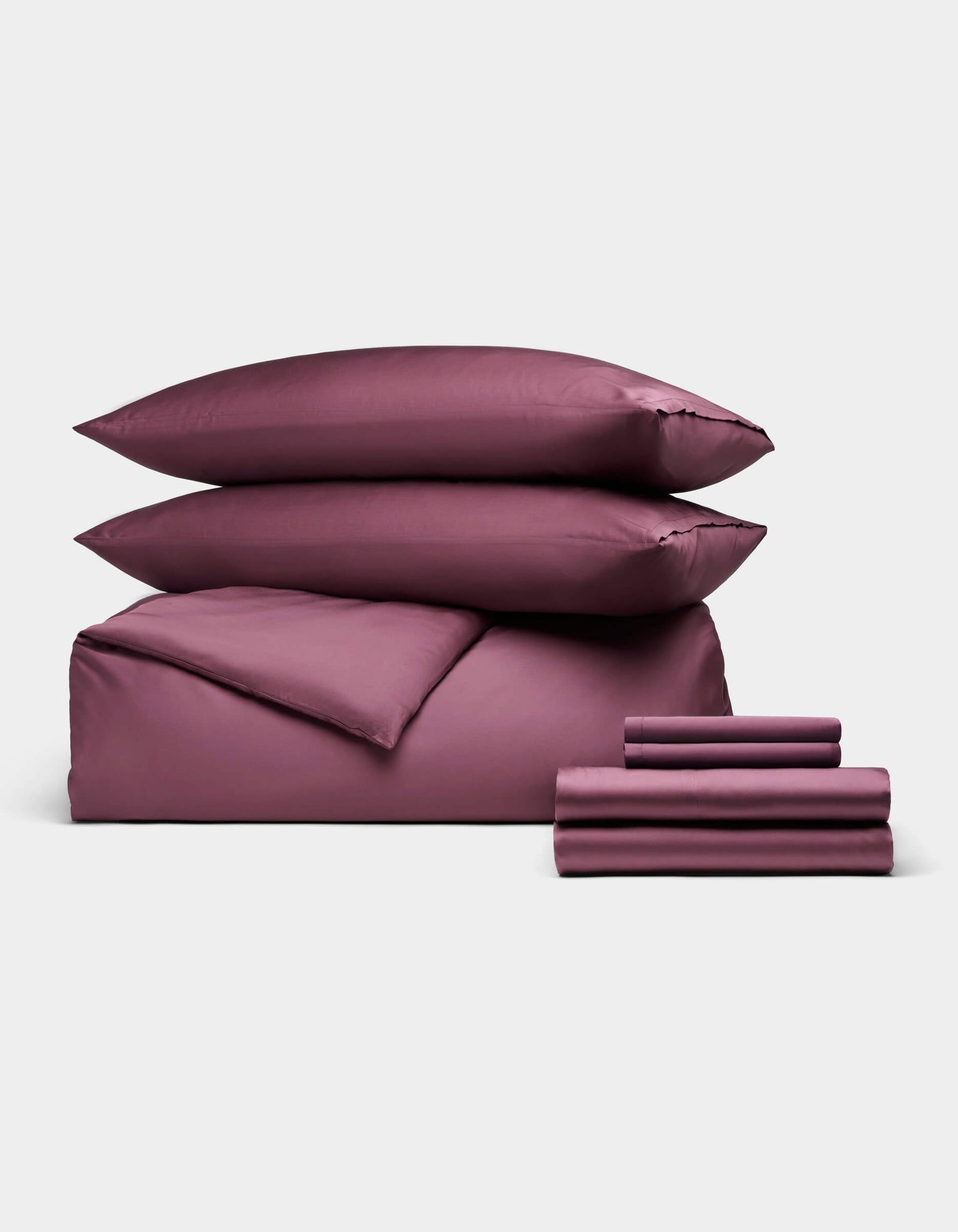 The Cozy Earth Bamboo Bedding Ultimate Bundle, featuring two pillows, a folded duvet, and stacked sheets in mauve, is neatly arranged against a plain white background.