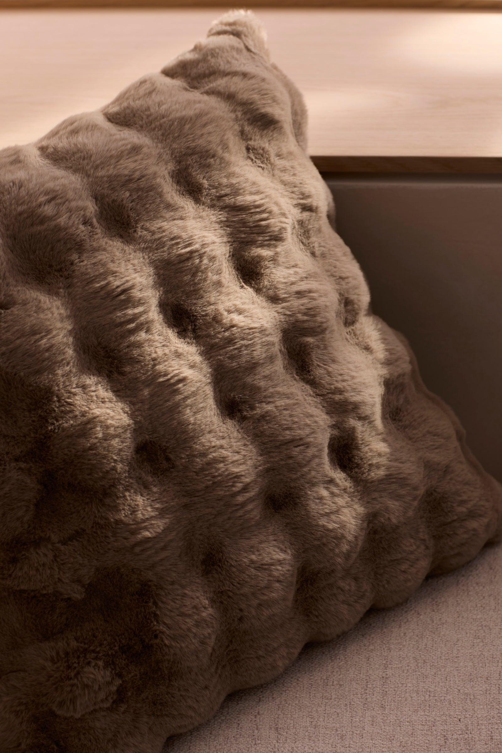 The Bubble Cuddle Pillow by Cozy Earth features a soft, brown, dimpled texture and rests against a neutral couch, adding comfort and style to any cozy indoor space. 