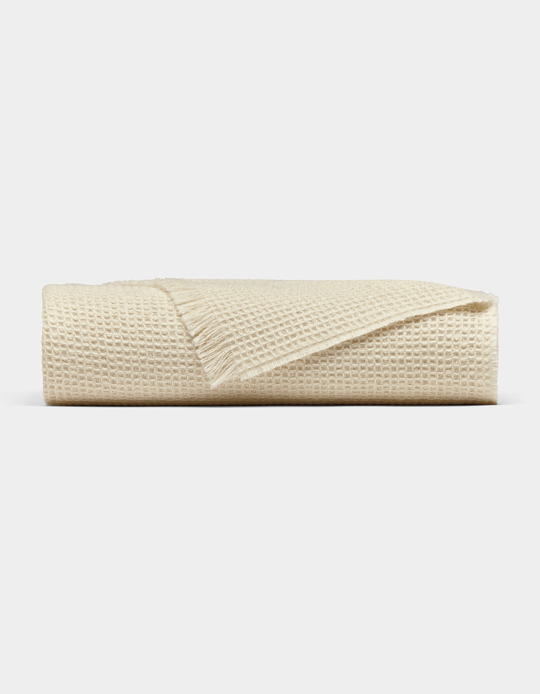 The Cozy Earth Alpaca Waffle Throw, in beige with a fringed edge, is neatly folded and displayed against a plain light gray background.