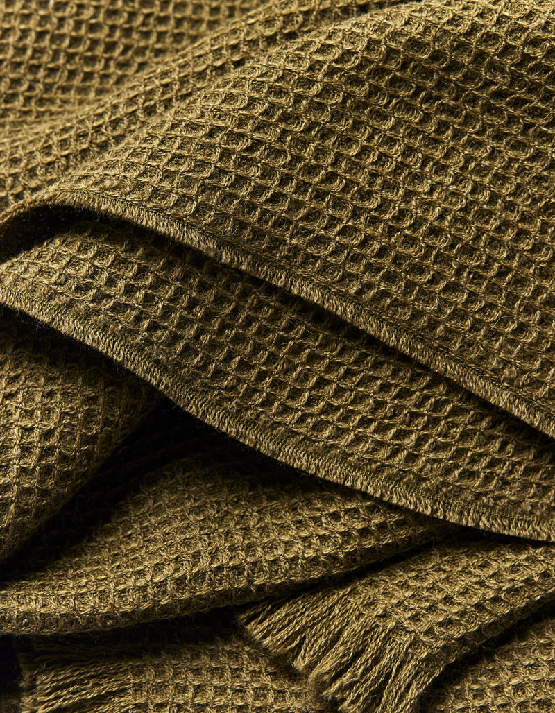 Close-up of the Cozy Earth Alpaca Waffle Throw, showcasing its textured olive green waffle weave, soft folds, and fringed edges.