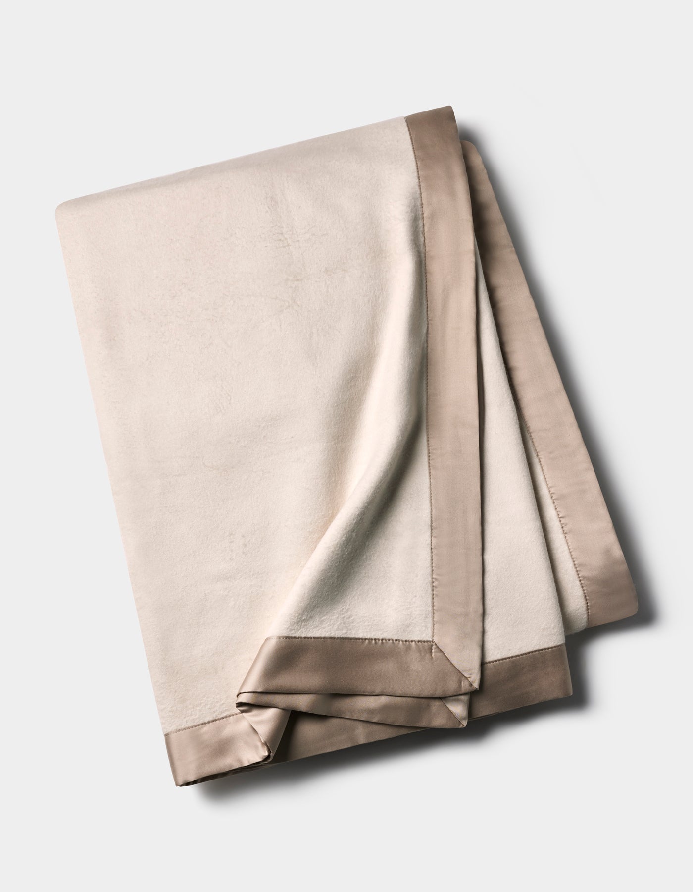The Cozy Earth Bamboo Blanket is folded and displayed on a neutral background, featuring an ivory color with a smooth, shiny taupe satin trim along the edges.