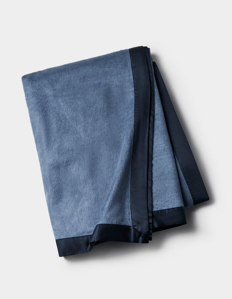 The Cozy Earth Bamboo Blanket, in blue with a dark satin trim, is shown folded against a plain light background.