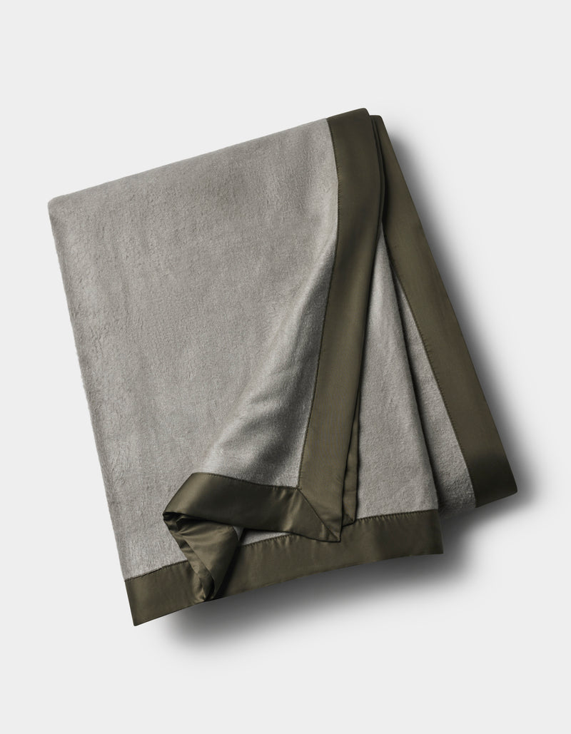 The Cozy Earth Bamboo Blanket, in light gray with a dark satin border, is neatly folded and displayed on a white background.