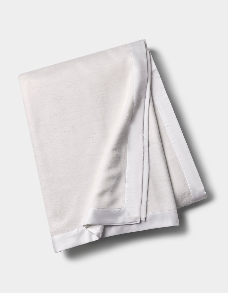 The Cozy Earth Bamboo Blanket, featuring a smooth satin border, is shown folded on a light gray background.