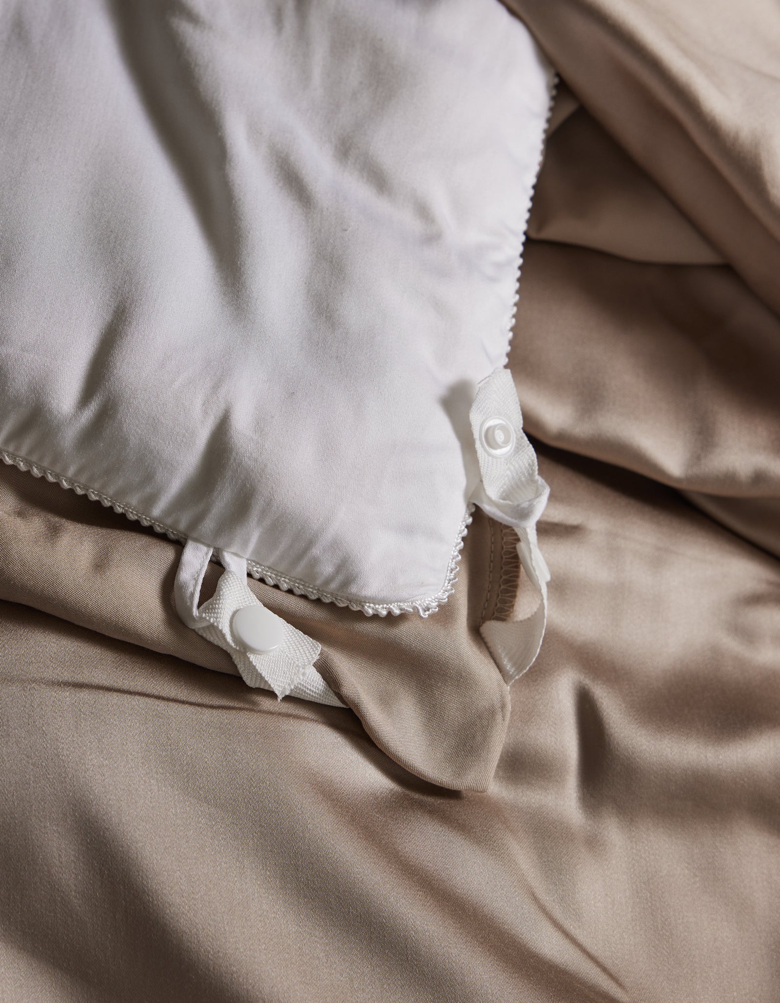 A close-up of Cozy Earth’s Bamboo Viscose Comforter with decorative trim and untied ribbon ties, resting on smooth, light beige sheets. The comforter's soft fabric appears slightly rumpled for a relaxed look.