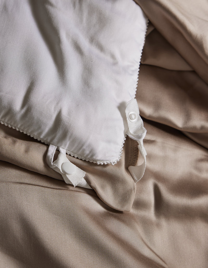 A close-up of the Cozy Earth Bamboo Viscose Comforter with decorative edges and fabric ties, resting on smooth beige bedsheets. The neatly fastened ties and soft bedding create an inviting look.