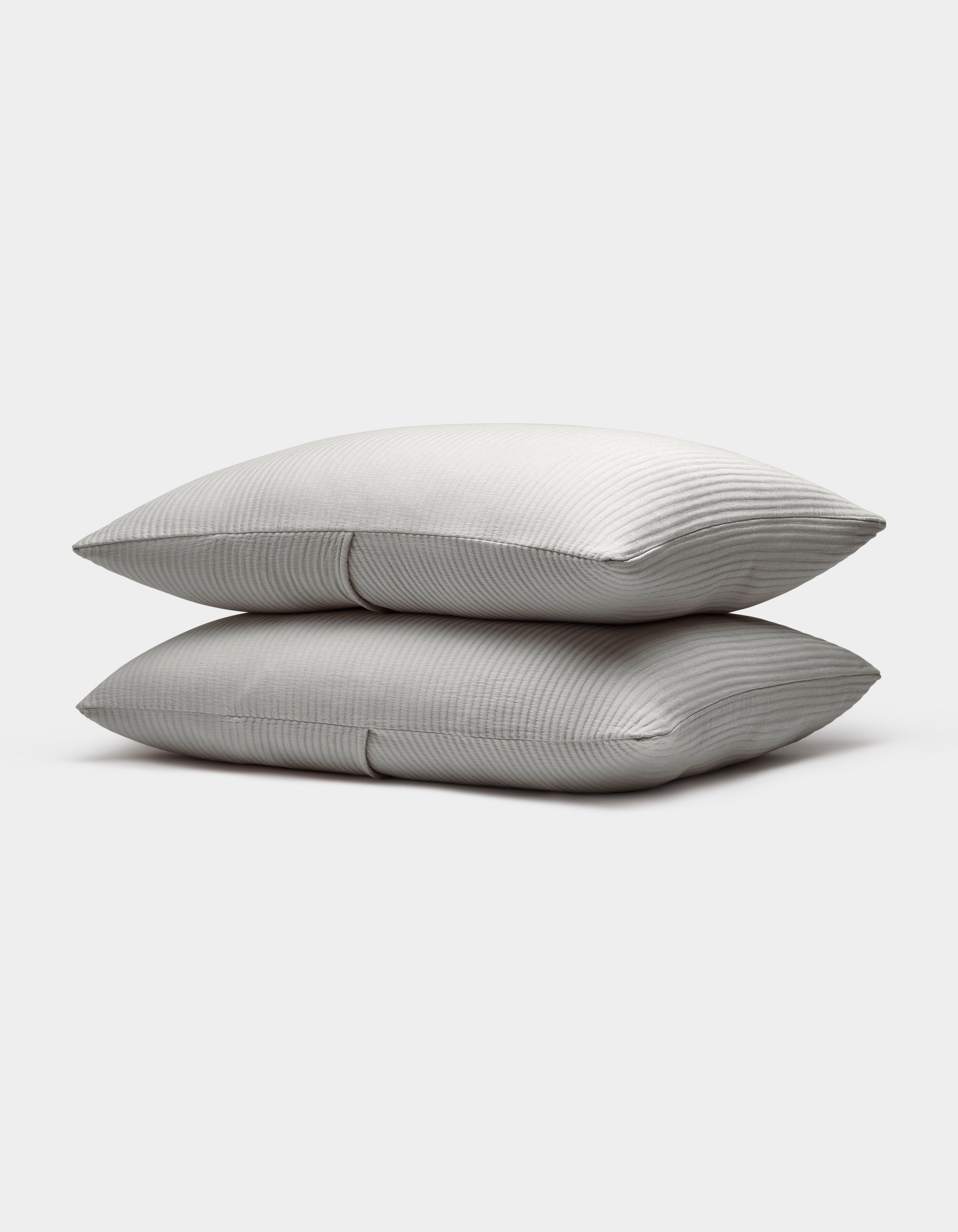 Two neatly stacked Bamboo Coverlet Shams by Cozy Earth, light gray with a subtle striped pattern, are displayed on a plain white background.|Color:Light Grey