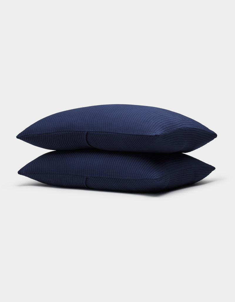 Two Bamboo Coverlet Shams by Cozy Earth, in dark blue with a subtle striped texture, are neatly stacked against a plain light gray background.