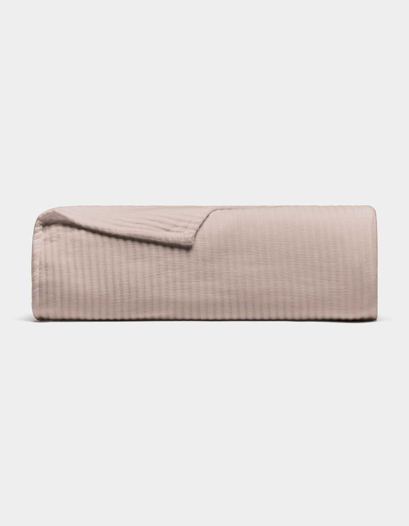 The Cozy Earth Bamboo Coverlet, shown folded in light beige with a subtle stitched texture, is displayed against a plain white background.