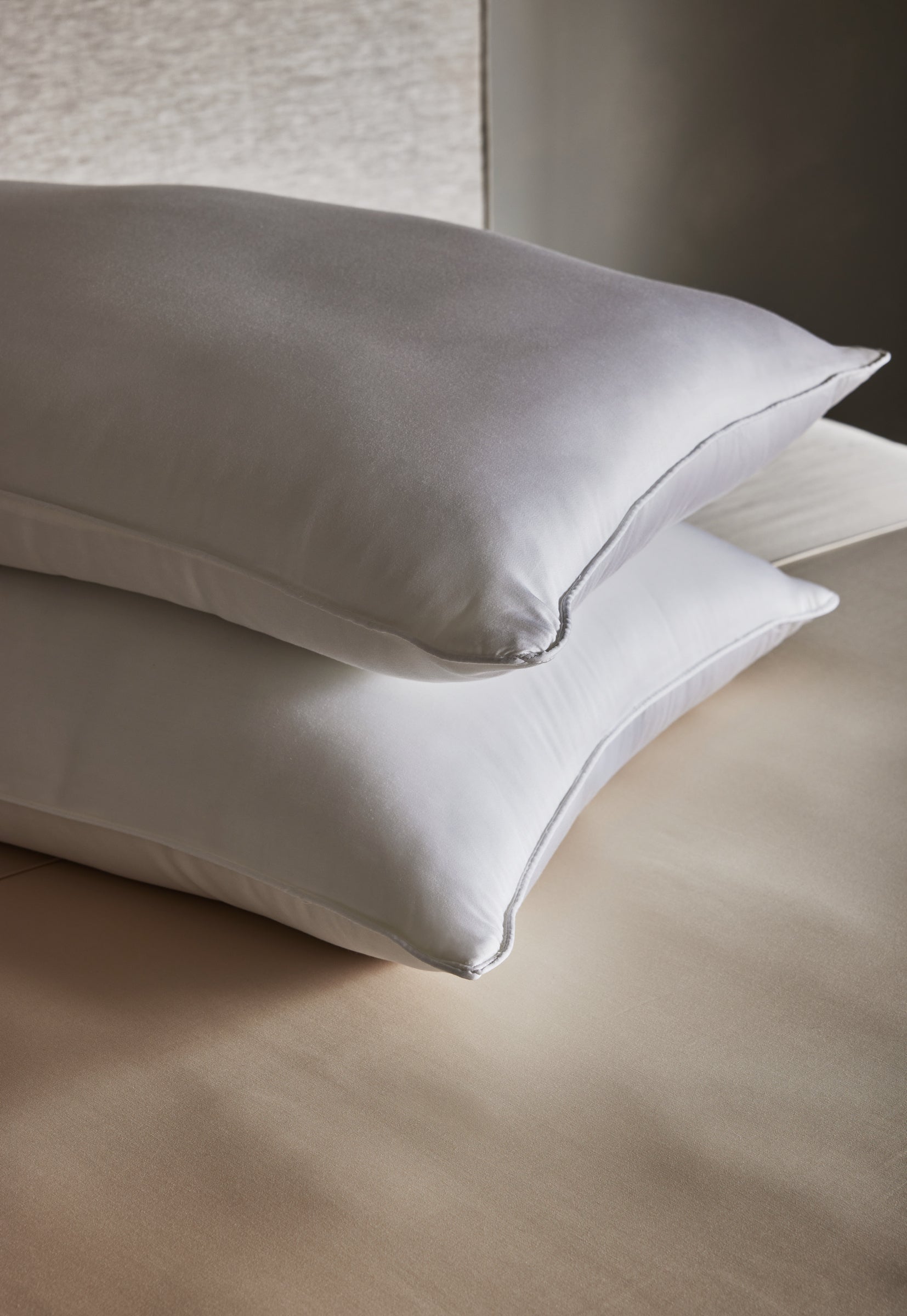 Two Cozy Earth Bamboo Down Alternative Pillows are neatly stacked on a beige bed with smooth, clean sheets, set against a neutral background.