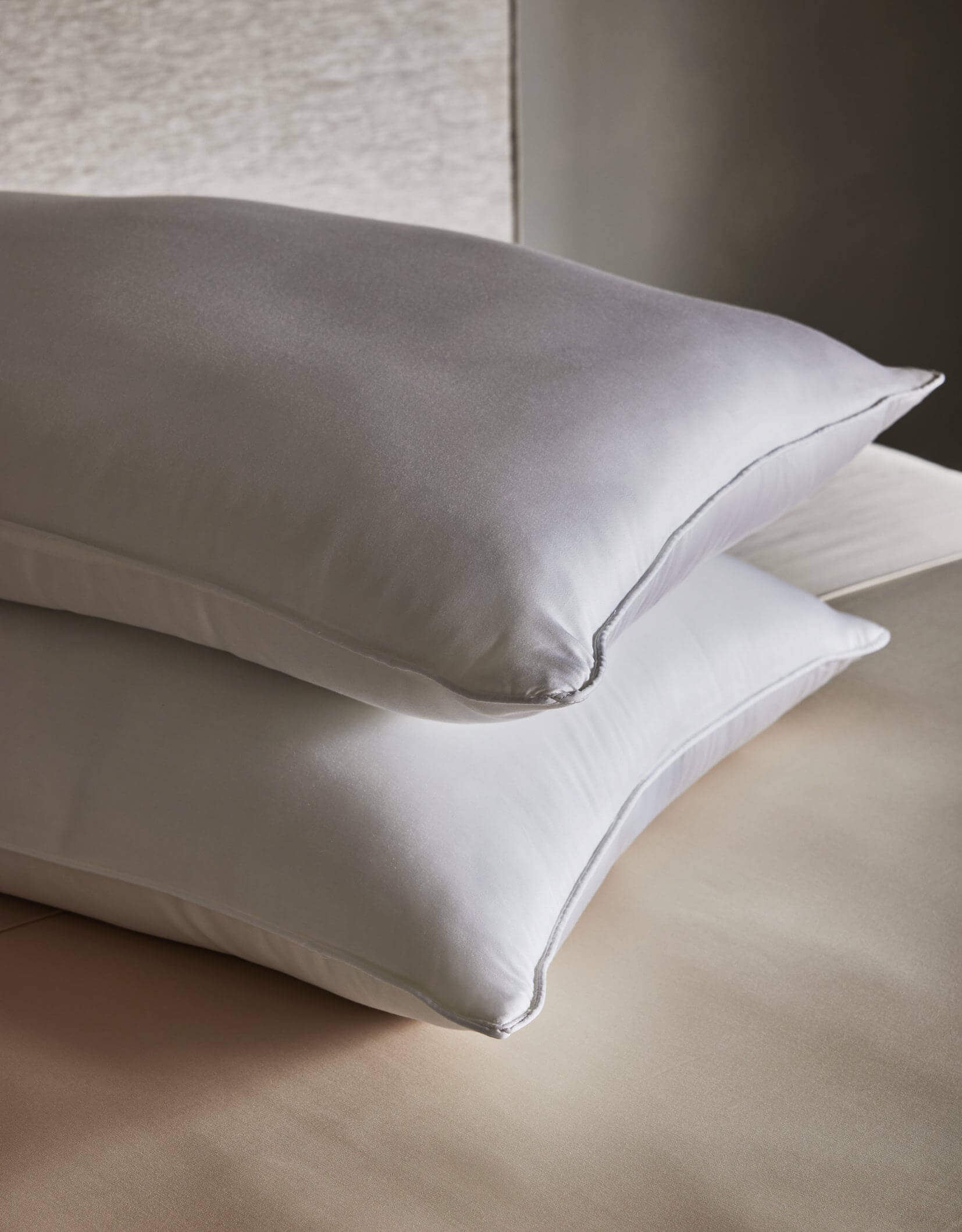 Two Cozy Earth Bamboo Insert Bundle pillows, crisp and white, are stacked neatly on a beige bed sheet in a softly lit room.