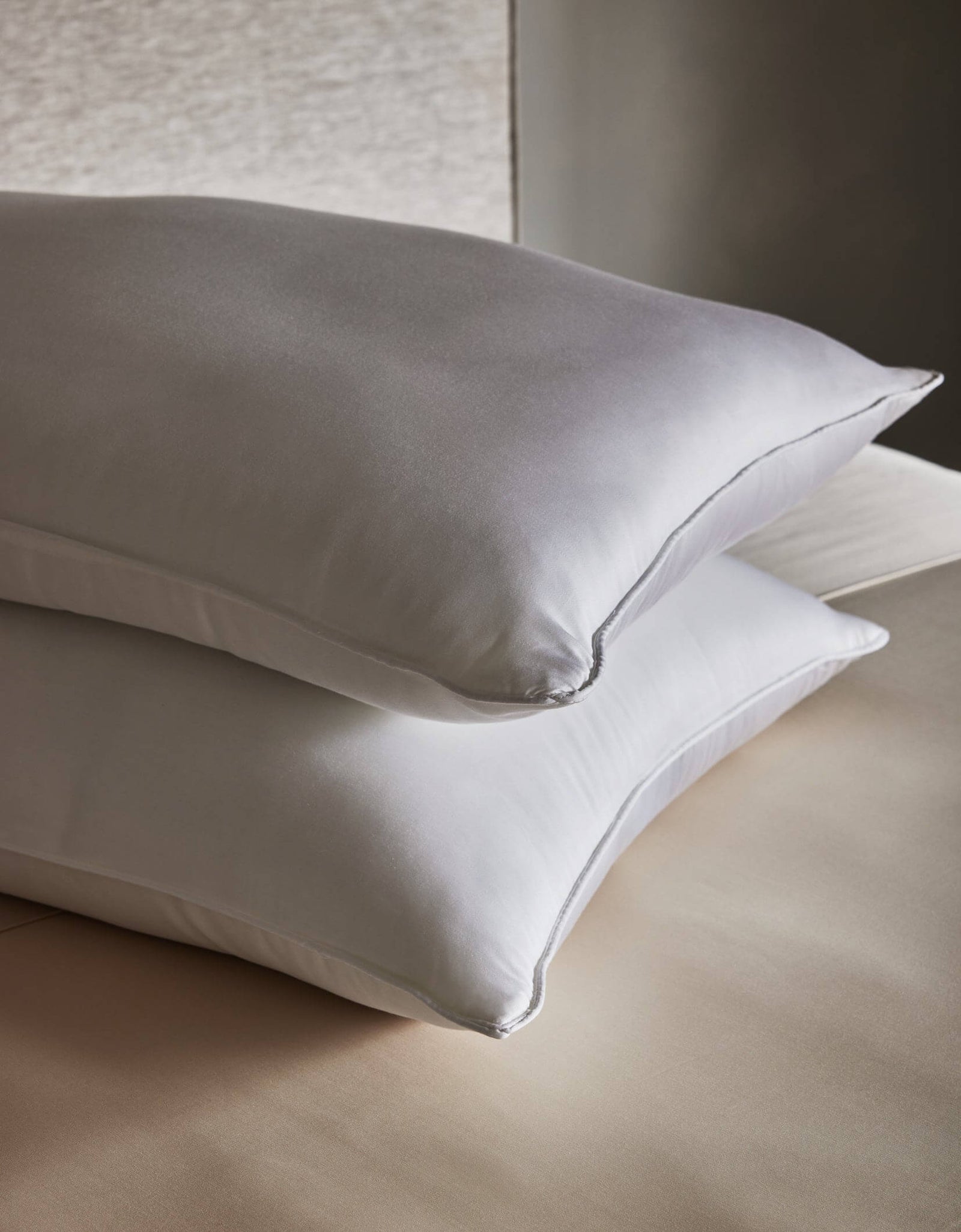 Two Cozy Earth Down Alternative Insert Bundle pillows in crisp white are stacked on a neatly made beige bed. A neutral wall in the background adds to the calm, minimalistic look.