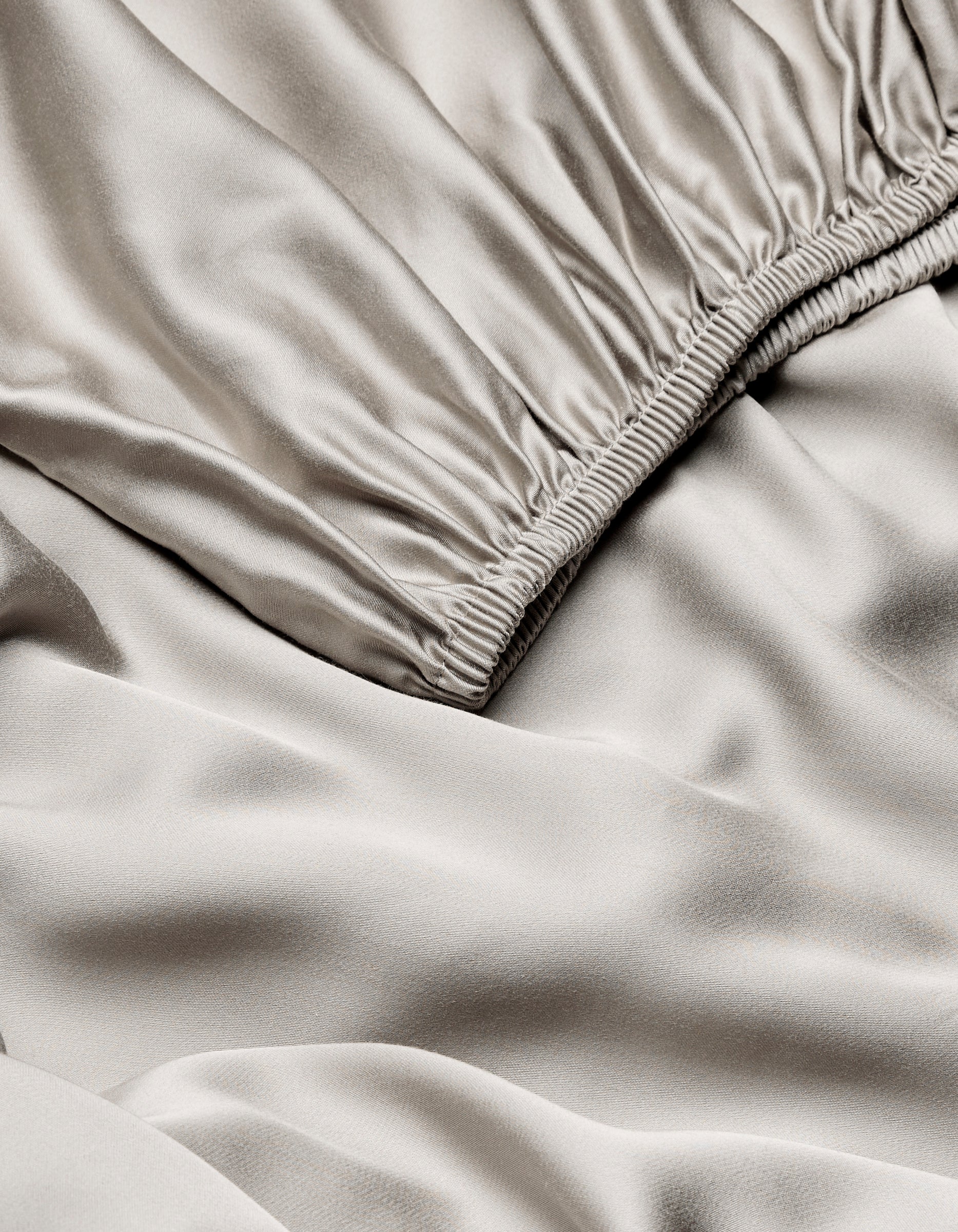 Close-up of Cozy Earth Bamboo Fitted Sheet in light beige, highlighting its smooth, shiny texture with gentle folds and ruching near the seam.