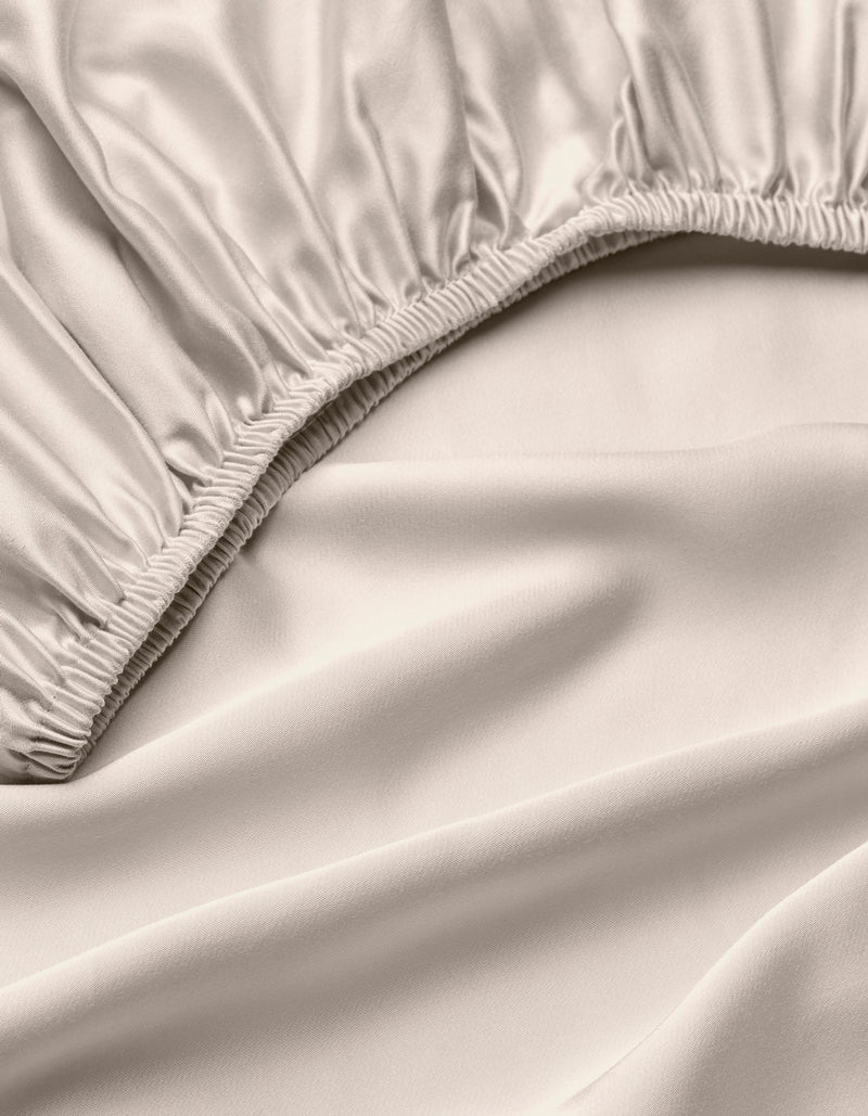 A close-up of the Cozy Earth Bamboo Fitted Sheet in light beige, highlighting its silky, smooth fabric, gathered elastic edges, and soft folds.