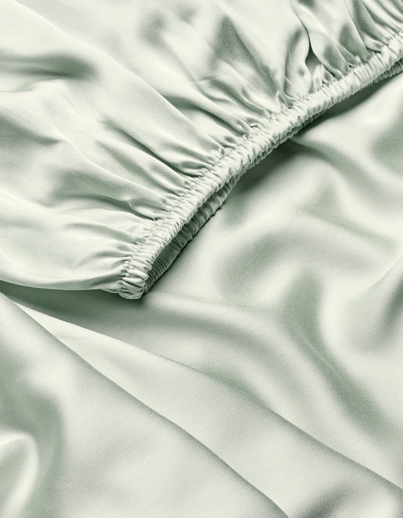 Close-up of Cozy Earth’s Bamboo Fitted Sheet in light green, showing silky fabric with a diagonal ruched seam that creates soft folds and a smooth, shiny texture.