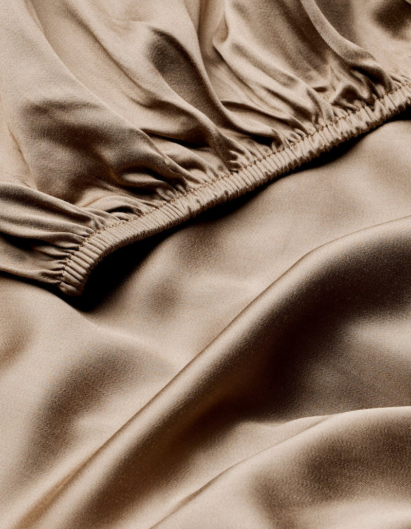 Close-up of Cozy Earth's Bamboo Fitted Sheet showcases its smooth, shiny beige fabric with gathered, ruched details and gentle folds for a soft, flowing texture.