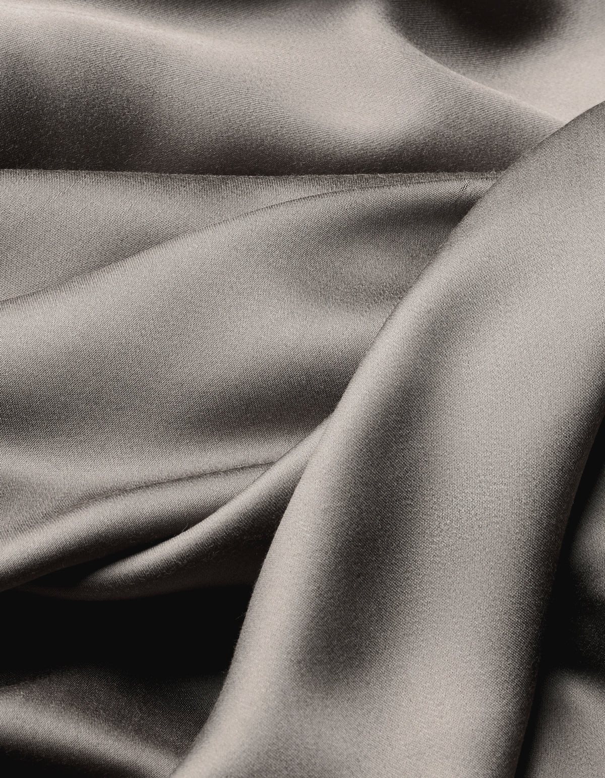Close-up of Cozy Earth's Bamboo Sheet Set reveals smooth, shiny silver-gray fabric with soft folds and flowing texture, offering a luxurious and elegant look.