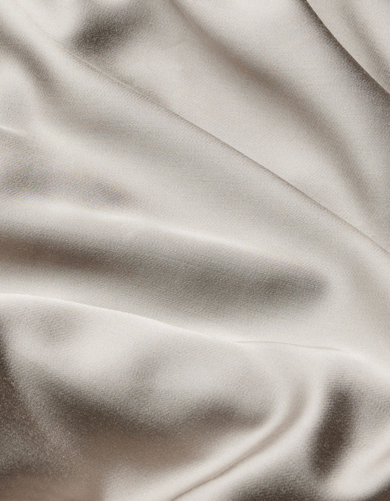 The Bamboo Flat Sheet by Cozy Earth features smooth, cream-colored satin fabric with gentle, flowing folds and a soft sheen that beautifully reflects light.