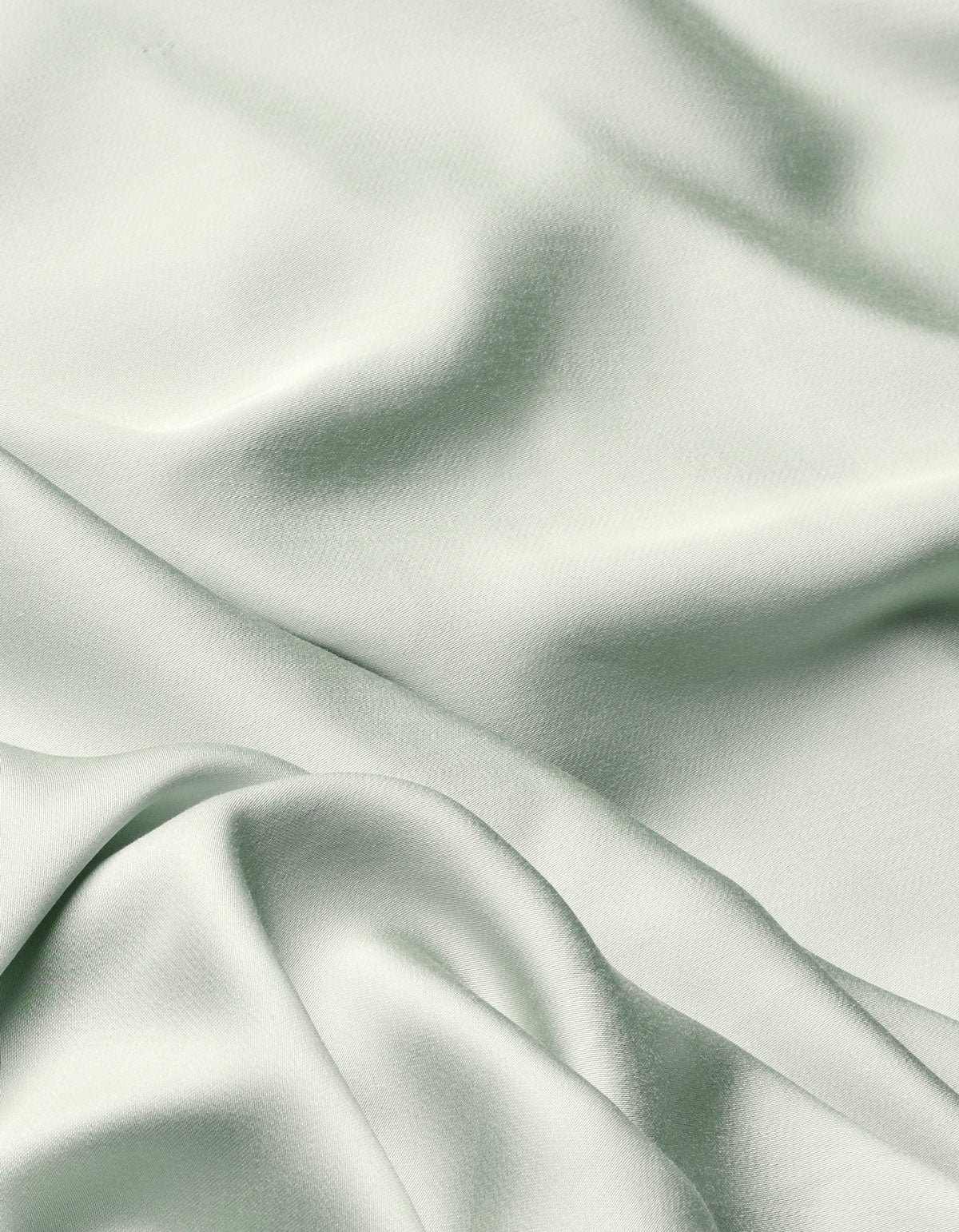 The Cozy Earth Bamboo Flat Sheet features a soft, light sage green fabric with a smooth texture and gentle folds that create subtle shadows and highlights across its surface.