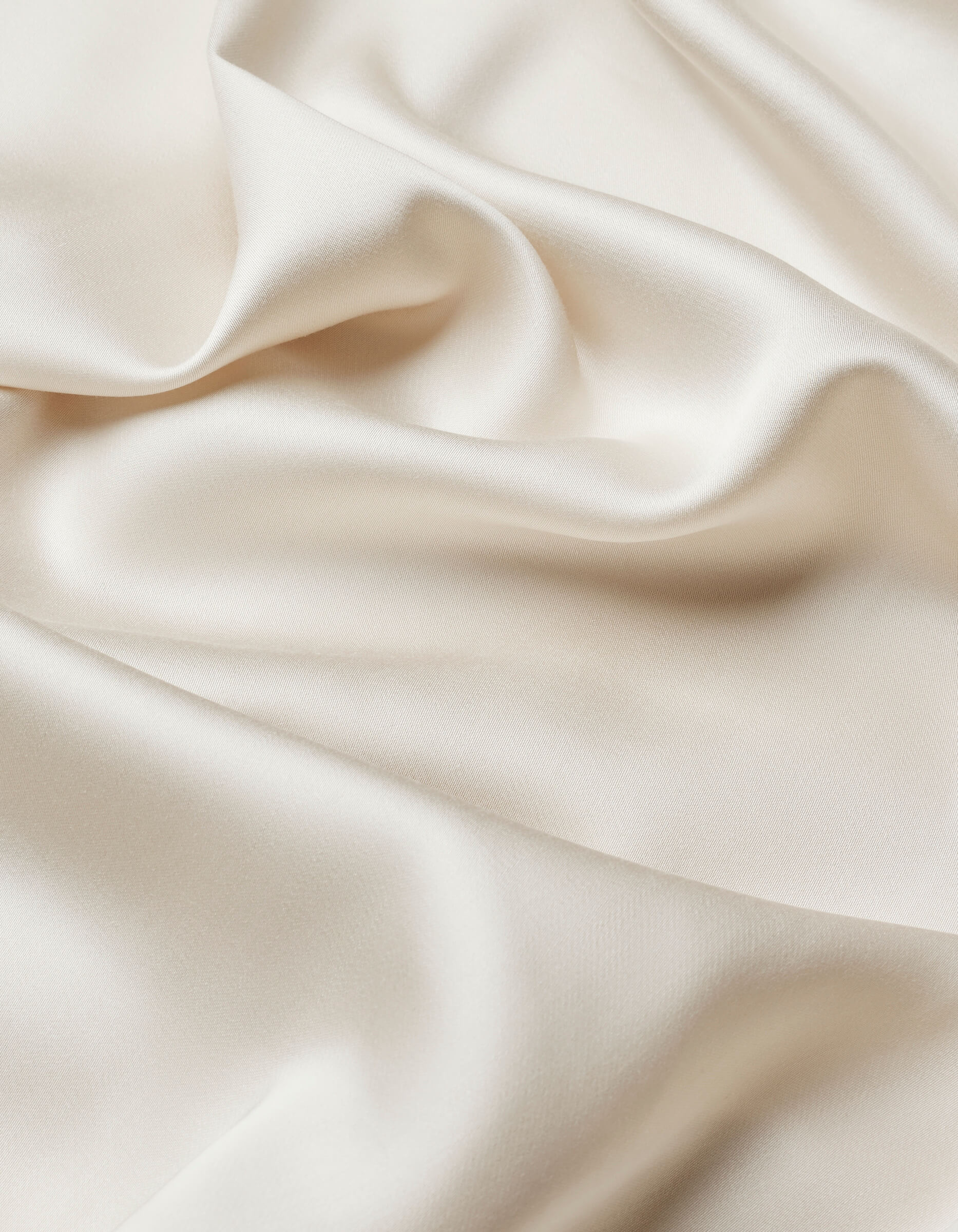 Close-up of Cozy Earth Bamboo Sheet Set in smooth, ivory satin with soft folds and gentle waves, showcasing its silky texture and subtle sheen.
