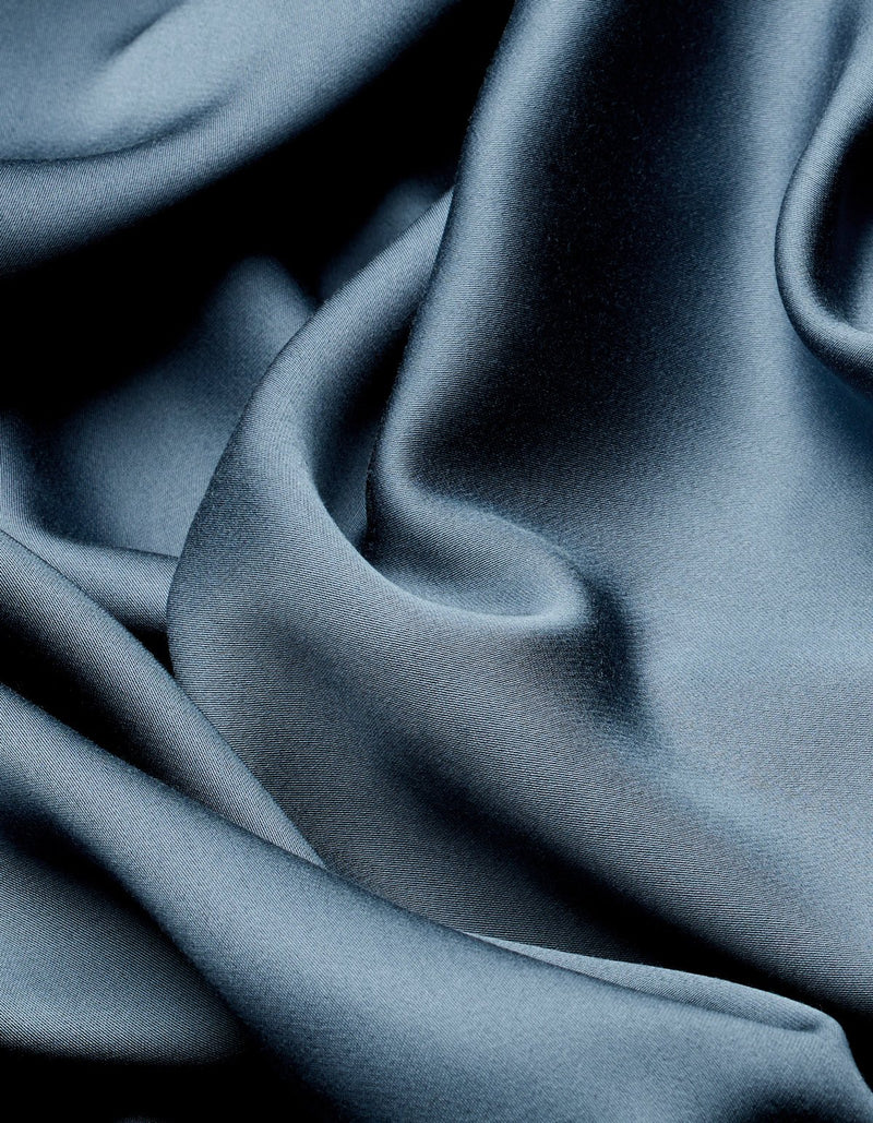 Close-up of the Cozy Earth Bamboo Flat Sheet in dark blue, featuring smooth, shiny fabric with soft folds and creases for a luxurious, elegant texture.