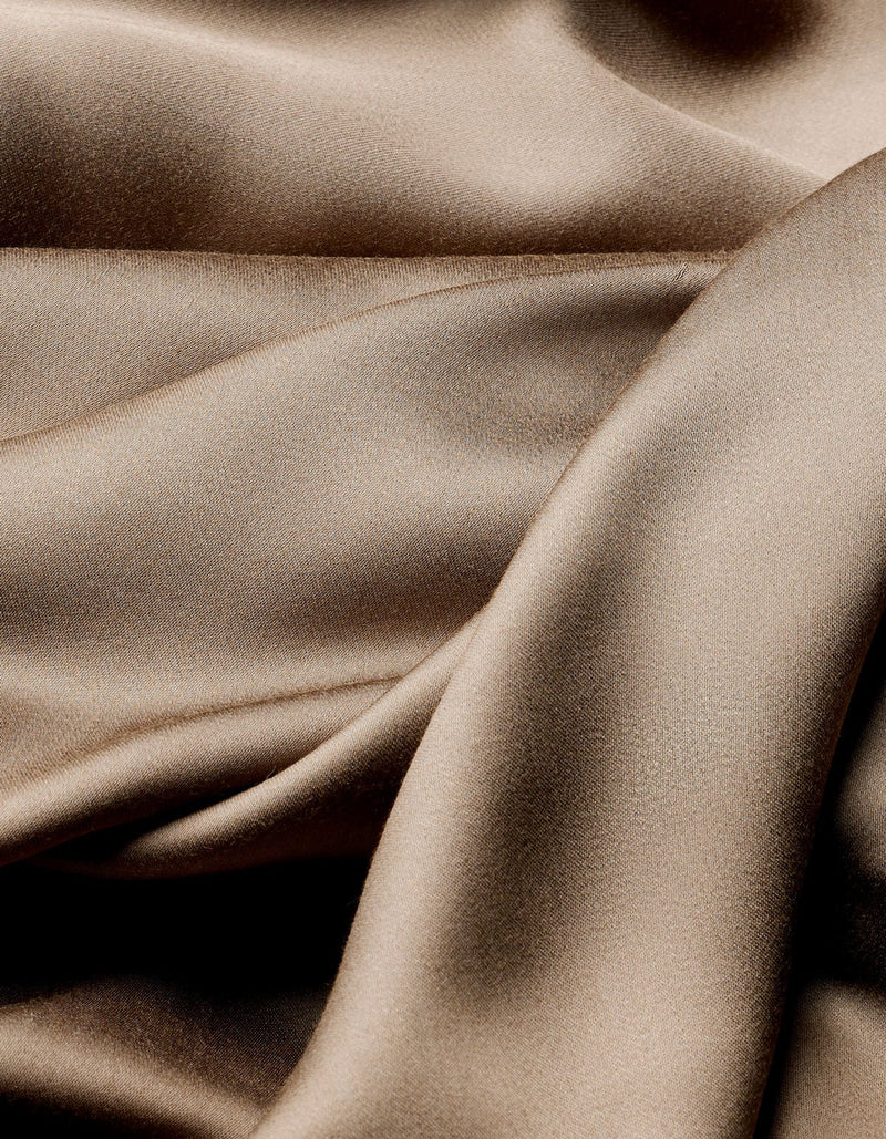 The Cozy Earth Bamboo Flat Sheet features smooth, light brown satin fabric with soft folds and gentle curves for a shimmering, luxurious texture.