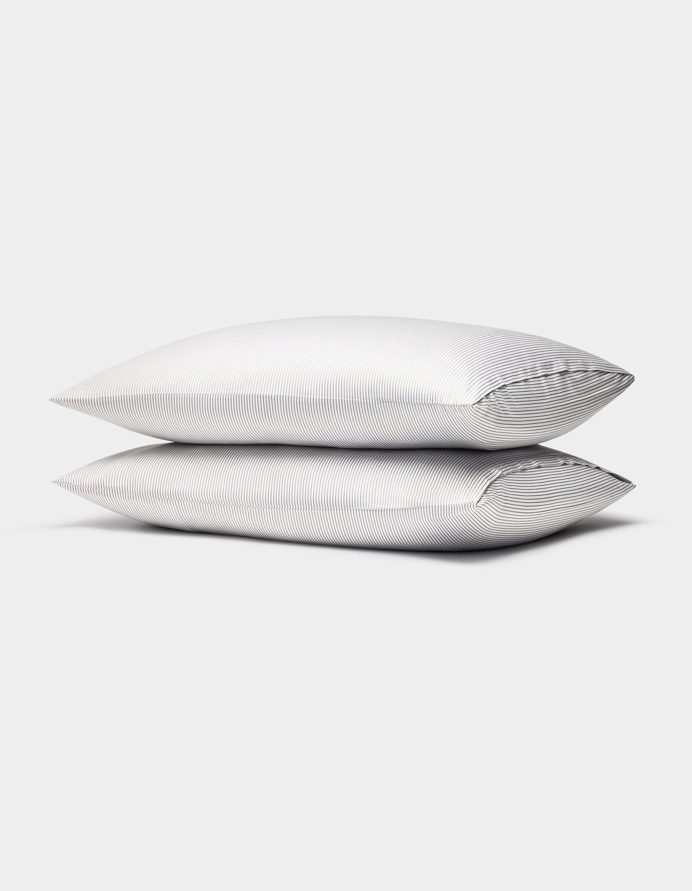Two Cozy Earth Bamboo Pillowcases, in white with subtle thin gray stripes, are stacked together against a plain light gray background.|Color:Charcoal Pinstripe
