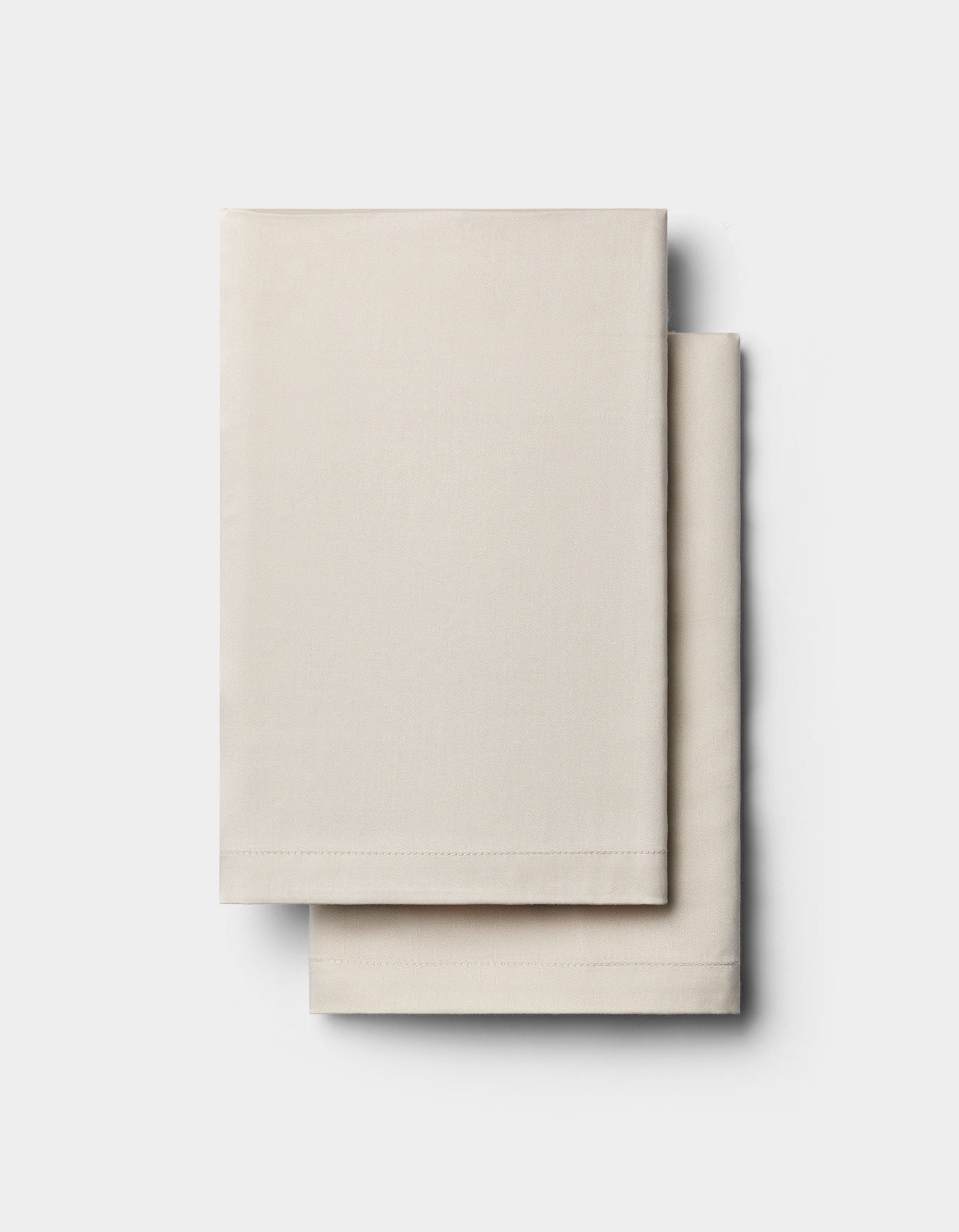 Two neatly folded, rectangular Bamboo Pillowcases by Cozy Earth in off-white are stacked atop each other against a light gray background.