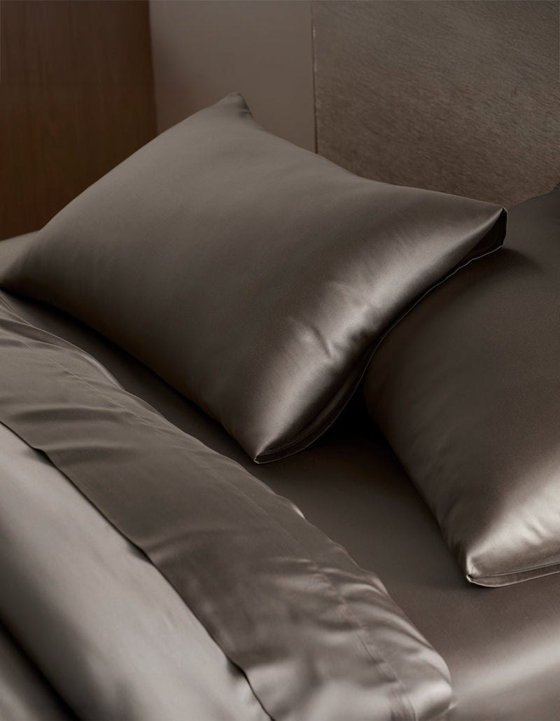 Two pillows and a neatly made bed are covered with smooth, dark brown Cozy Earth Bamboo Pillowcases, giving the bedding a soft and luxurious appearance.