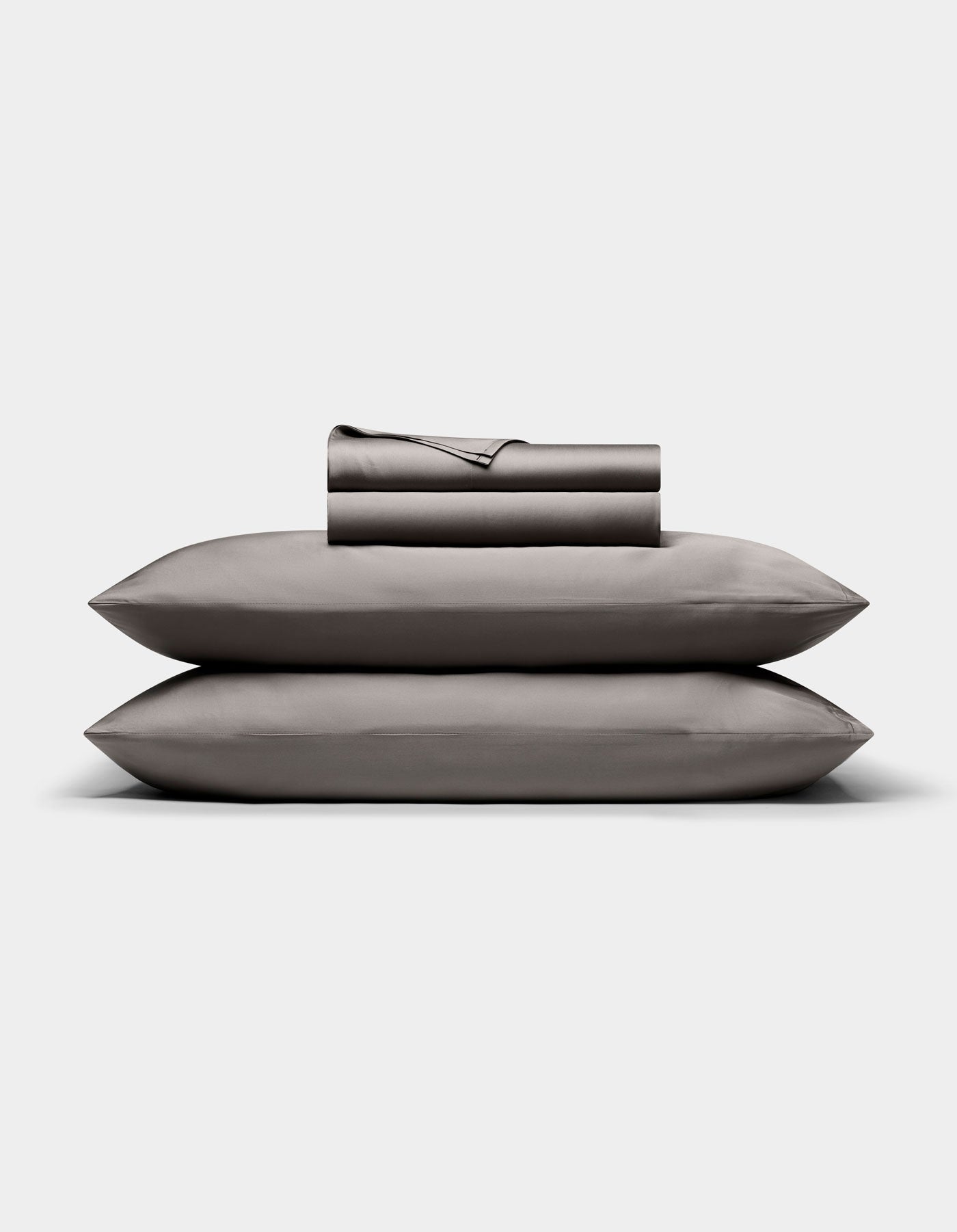 The Cozy Earth Bamboo Sheet Set, in dark gray, is neatly folded with matching pillowcases stacked atop two pillows, all arranged against a plain white background.