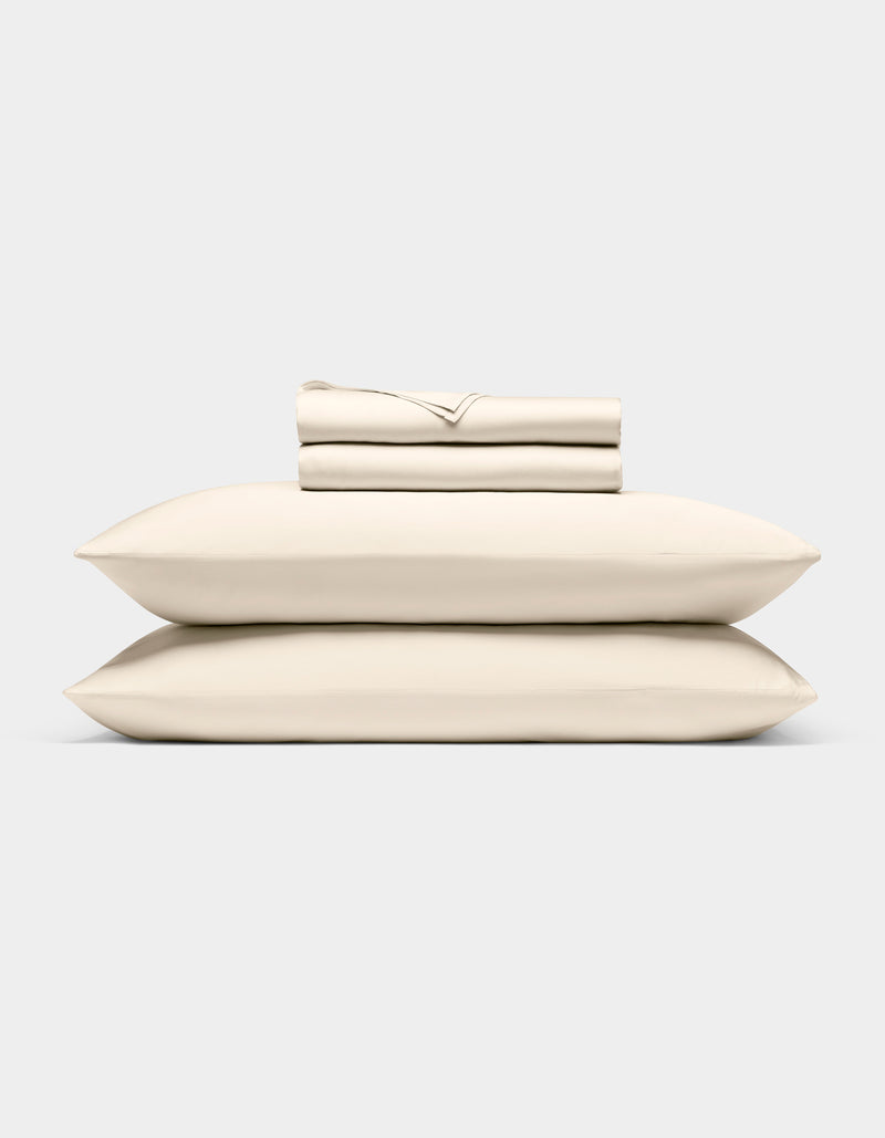 The Cozy Earth Bamboo Sheet Set, neatly folded in cream, rests atop two matching pillows against a light gray background.