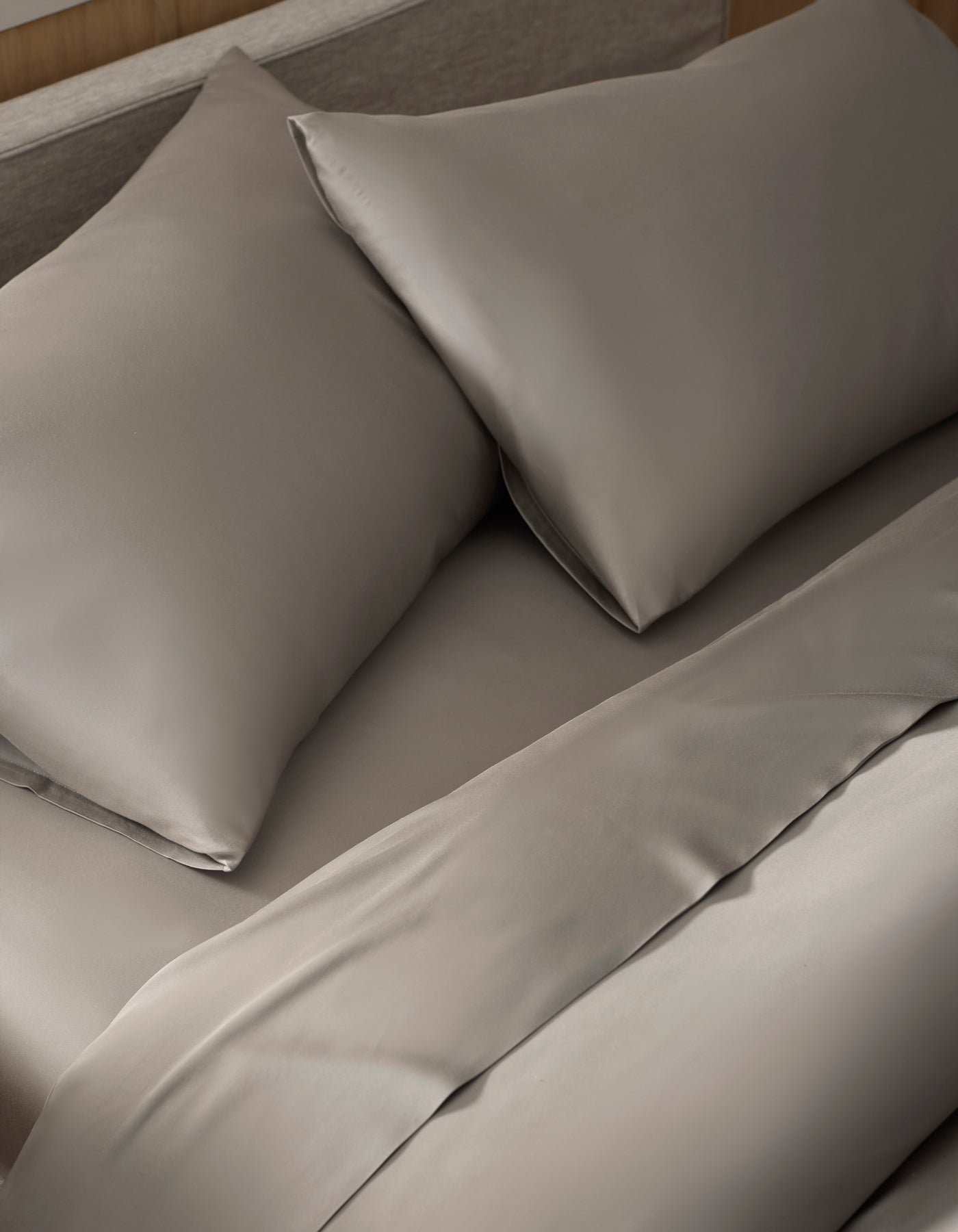 A close-up view of a neatly made bed with taupe Bamboo Pillowcases by Cozy Earth, featuring a smooth, soft-looking fabric.