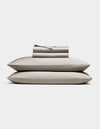 The Cozy Earth Bamboo Sheet Set, in light gray, includes neatly folded bed sheets and pillowcases stacked atop two pillows, all shown against a plain white background.|Color:Dove Grey
