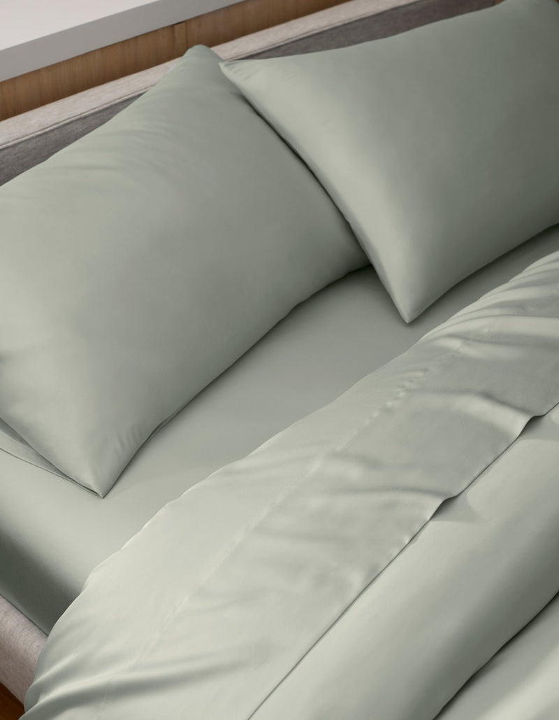 A neatly made bed features light gray Cozy Earth Bamboo Pillowcases, with two pillows propped against the headboard. The bedding appears smooth and soft.