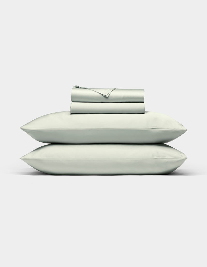 The Cozy Earth Bamboo Sheet Set, in light gray, features neatly folded bed sheets with two matching pillowcases stacked on top, displayed against a plain white background.
