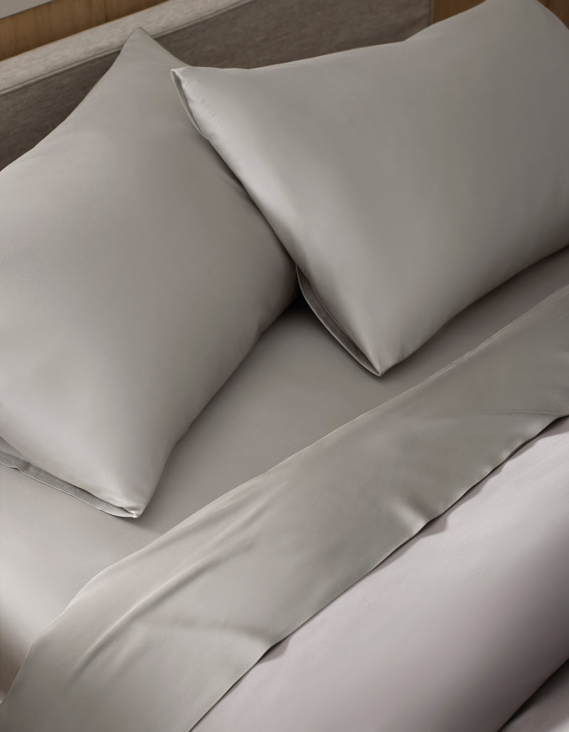 A close-up of a neatly made bed featuring the Bamboo Sheet Set by Cozy Earth in light gray, with matched pillows for a clean and elegant appearance.
