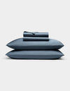 A neatly folded Cozy Earth Bamboo Sheet Set, featuring a fitted sheet, flat sheet, and two pillowcases, is stacked atop two matching blue pillows against a plain white background.|Color:Pacific Blue
