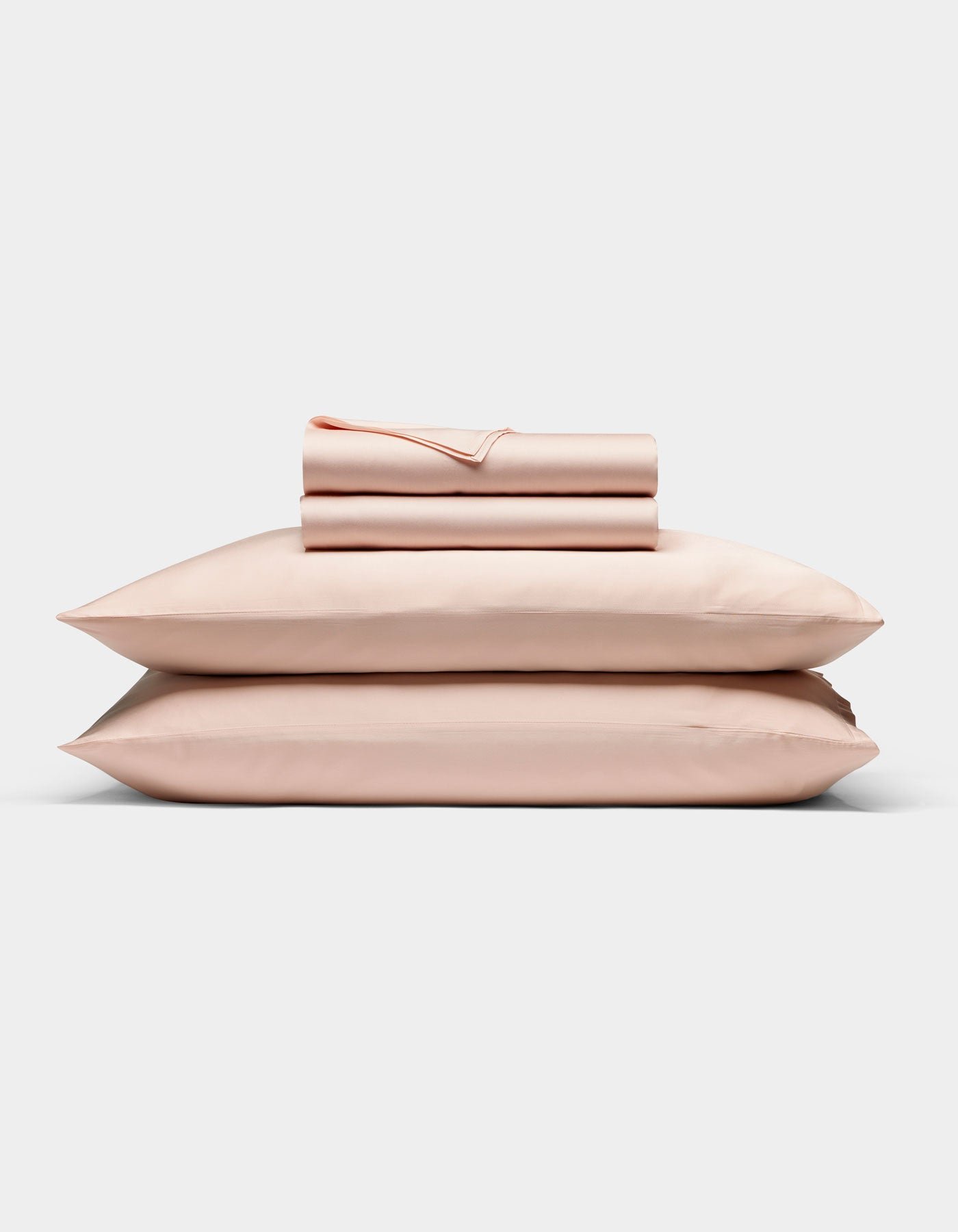 The Cozy Earth Bamboo Sheet Set in light pink is neatly folded with matching pillowcases, stacked on two pillows against a plain white background.