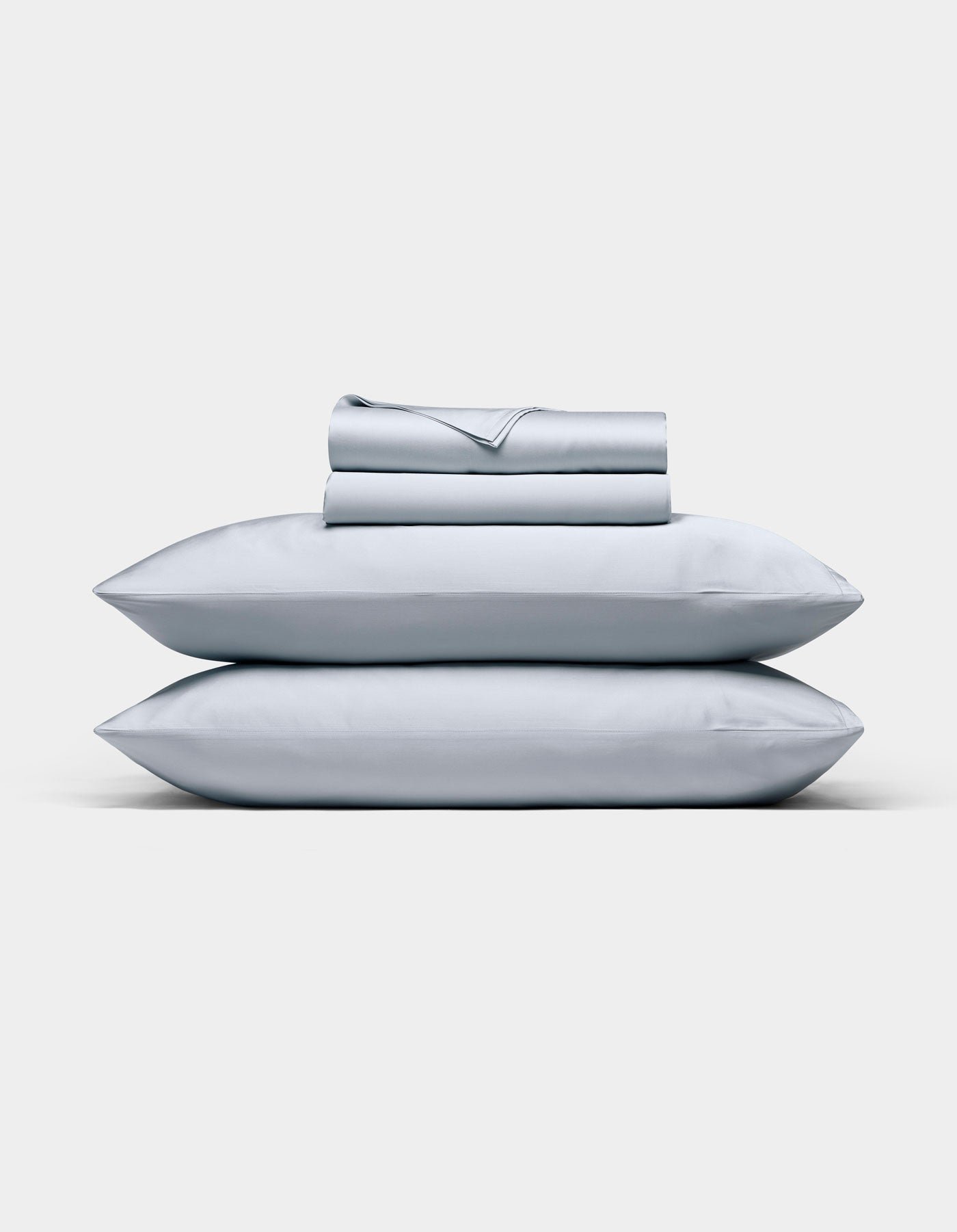 A neatly folded Cozy Earth Bamboo Sheet Set in light gray, with matching pillowcases stacked on two pillows, displayed against a plain white background.