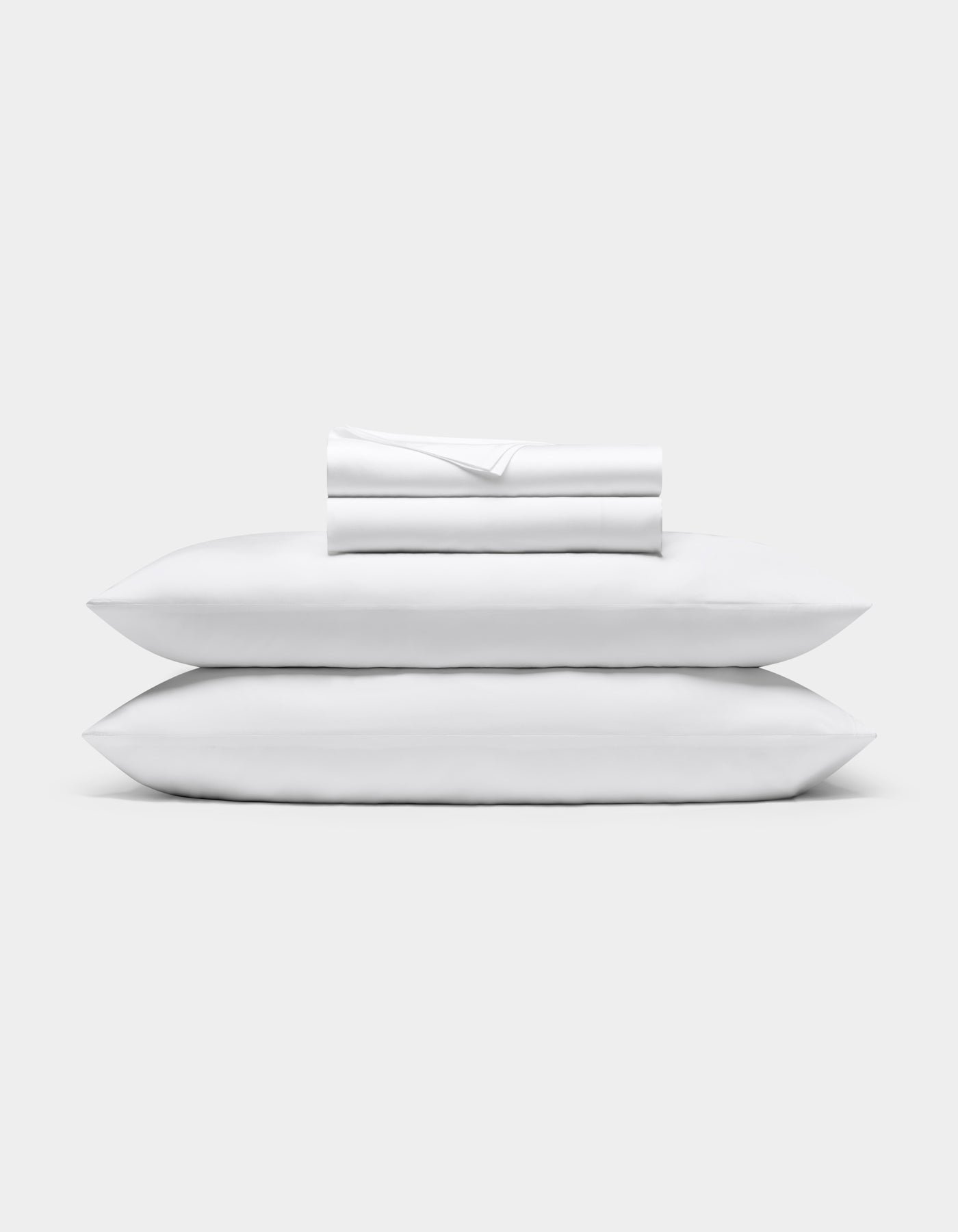 A neatly folded Bamboo Sheet Set by Cozy Earth is stacked on two white pillows, all set against a plain light gray background.|Color:White