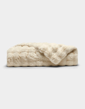 The Cozy Earth Bubble Cuddle Blanket is a folded, cream-colored faux fur throw with a soft, plush texture, shown against a plain white background.|Color:Creme