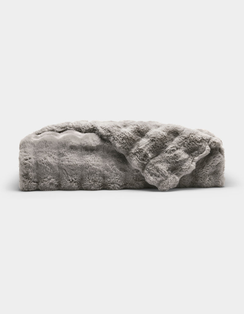 The Bubble Cuddle Blanket by Cozy Earth is a plush, light gray faux fur throw with a soft, textured surface, shown folded and partially draped open against a plain white background.